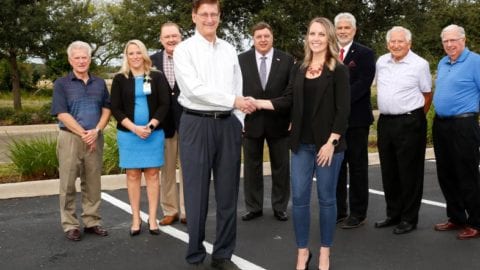 Village Manager Steve Sarkozy and Estero Chamber CEO Sarah Newcomb shake hands, signifying partnership, surrounded by representatives of other organizations involved in economic development